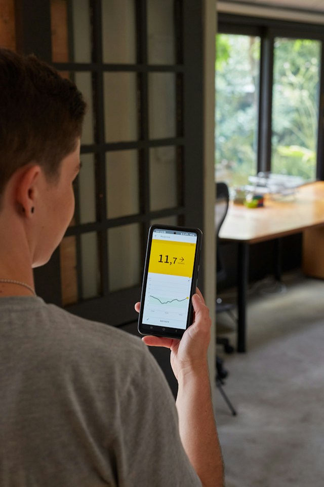 As we connect more devices to our home networks, we need to look closely into data privacy for sustainable home living. person looking at smartphone to adjust smart home settings in dining room